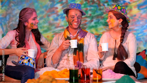 Cheerful Indian teenagers smeared in powder color and celebrating joyful Holi Festival - Gulal Colorful. Group of young friends wishing each other "Happy Holi" while having tea and Gujjia - festi...