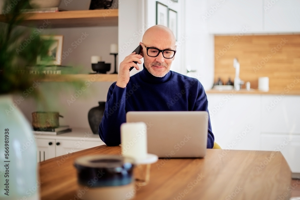 Middle age businessman sitting at home and using laptop and mobile phone for work