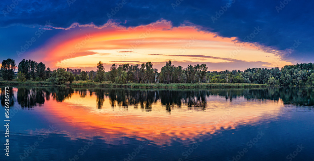 Sunset on the lake. Orange clouds on the background of the blue sky are illuminated by the sun