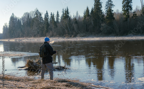 Man with a fishing rod next to river in cold weather.