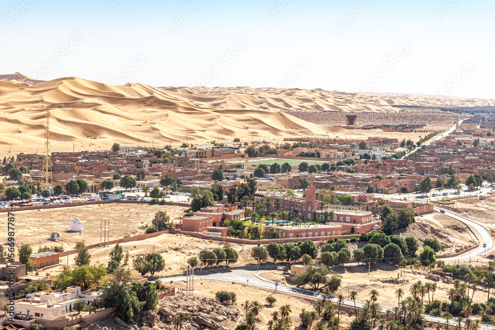 Elevated view from Baroun mountain in Taghit, Bechar. Sahara desert of Algeria with the Saoura hotel building and swimming pool, a mosque minaret and a soccer field. Trees, palm trees, and sand dunes.