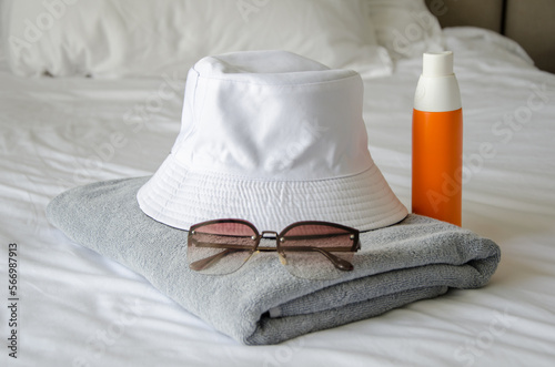 Preparing to visit beach. There is towel, panama, sunglasses and sun spray on bed. Sun protection. photo