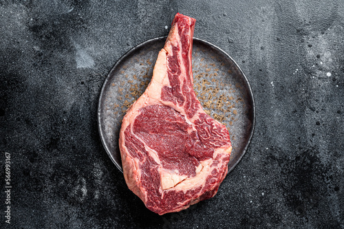 Raw cowboy steak, rib eye steak with bone, beef marbled meat on butcher cutting board. Black background. Top view. Copy space photo