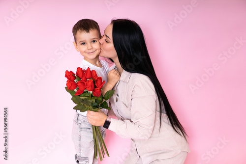 mom kisses a happy son, the son gave mom a bouquet of roses congratulating her on mother's Day during the celebration of the holiday on a pink background.