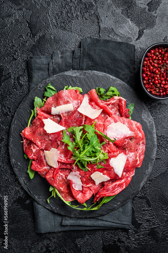 Beef carpaccio with arugula, parmesan cheese. Black background. Top view
