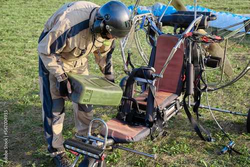 Professional paraglider in a helmet refuels the paraglider engine with fuel from a canister before the flight. A paraglider equipped with an engine must be refueled with kerosene for flight