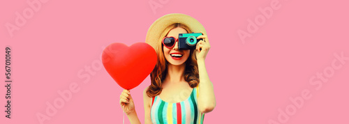 Summer portrait of happy smiling young woman with film camera and red heart shaped balloon wearing straw hat on pink background, blank copy space for advertising text © rohappy
