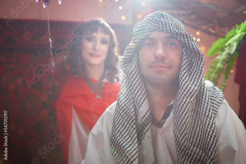 Portrait of young arabian muslim couple in traditional clothes in cozy red room. Fhoto shoot in easten style with male and female model like in a harem with a sultan and an odalisque