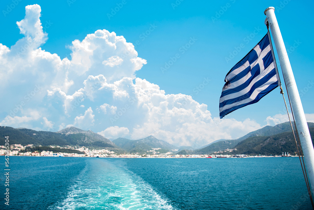 National flag of Greece on a ferry on the background of Greek island landscapes and the trace of the ferry on the water of the sea.