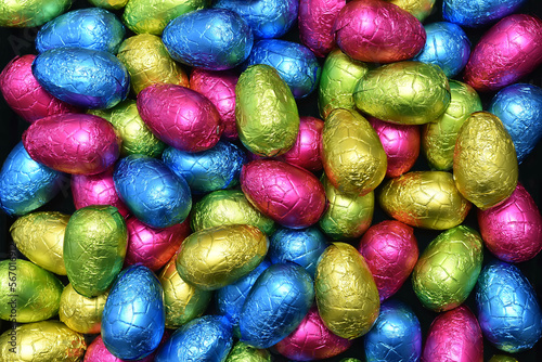 Pile or group of multi colored colourful foil wrapped chocolate easter eggs in pink, blue, yellow and lime green.