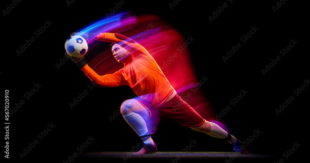 Fototapeta premium Sportive energetic man, soccer football goalkeeper in action, motion over dark background with mixed neon light. Concept of sport, achievement, competition, goals.