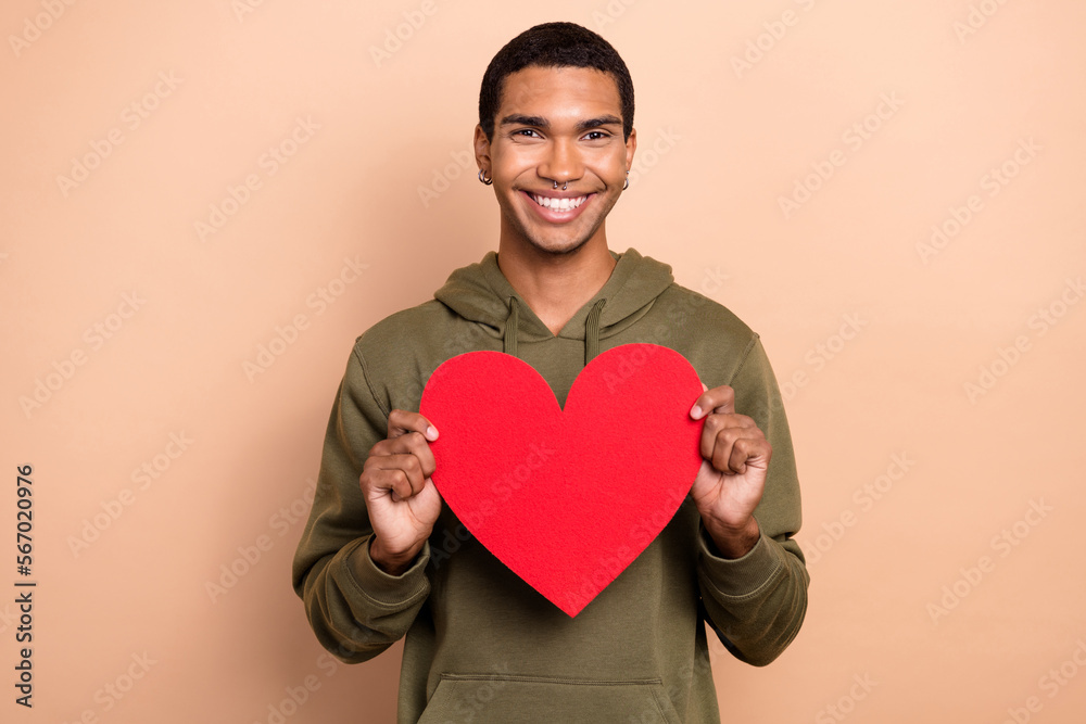 Photo of young cheerful satisfied optimistic guy hold red paper postcard valentine day gift present for girlfriend isolated on beige color background Photo of young cheerful satisfied optimistic guy hold red paper postcard valentine day gift present for girlfriend isolated on beige color background