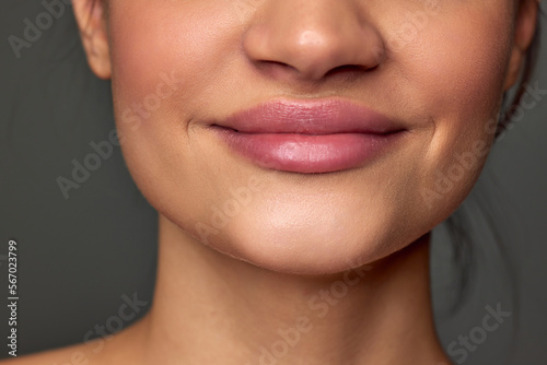 Cropped image of female face, lips, nose, chin on grey studio background. Lip augmentation, face lifting, plastic surgery. Concept of natural beauty, skin care, cosmetology, cosmetics, health, fashion