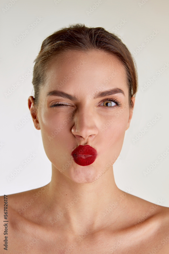Kisses. Young beautiful brunette girl with red lips posing over grey studio background. Femininity. Concept of natural beauty, skin care, cosmetology, cosmetics, health, fashion, plastic surgery Kisses. Young beautiful brunette girl with red lips posing over grey studio background. Femininity. Concept of natural beauty, skin care, cosmetology, cosmetics, health, fashion, plastic surgery