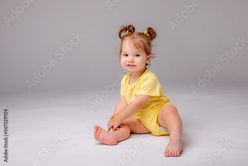 baby girl with yellow bodysuit sitting on a white background