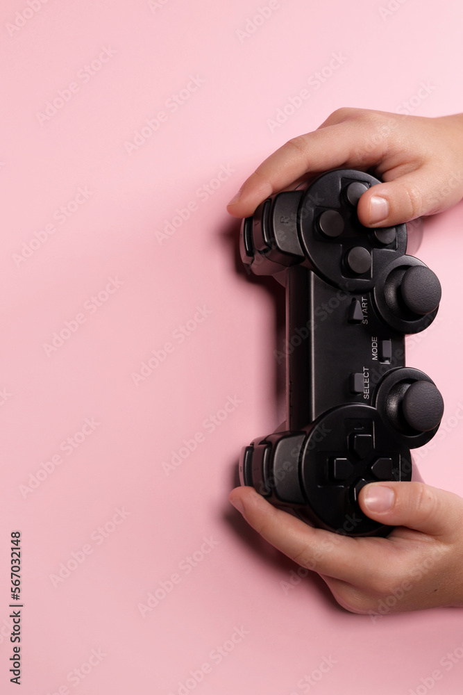 Children's hands hold a joystick, gamepad, playing video games on a pink background. Vertical Orientation Children's hands hold a joystick, gamepad, playing video games on a pink background. Vertical Orientation
