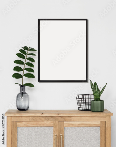 Empty vertical frame mockup in modern minimalist interior with plant in trendy vase on white wall background, Template for artwork, painting, photo or poster