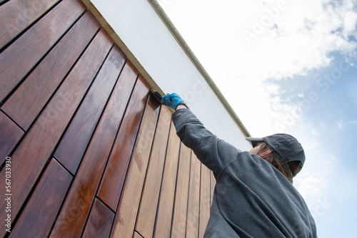 Staining the wood facade cladding with paint brush and protective oil, stain, house improvement copy space, looking up perspective angle