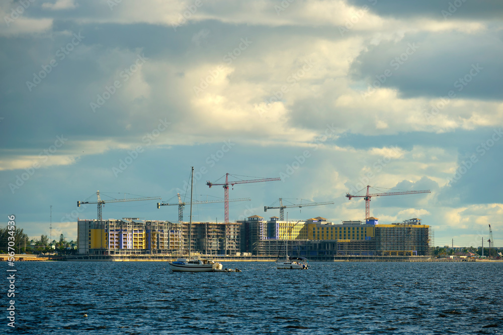 Tower cranes and frame structure of high residential apartment buildings at construction site on sea bay shore. Real estate development at waterfront