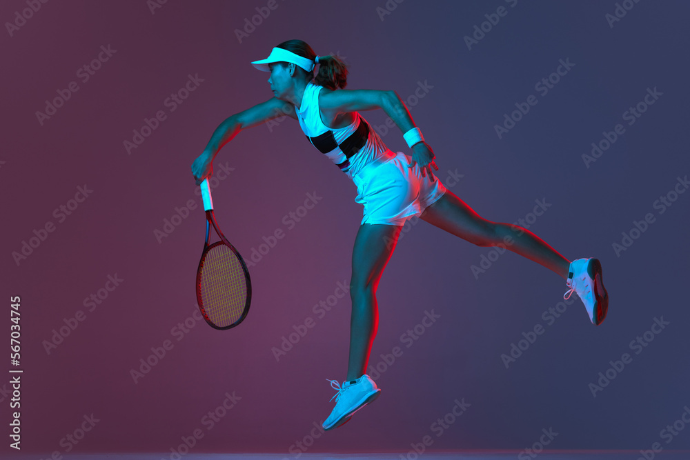 Back view of professional tennis player playing tennis over pink-purple background in neon light. Concept of sport, health, strength, action, motion, lifestyle.