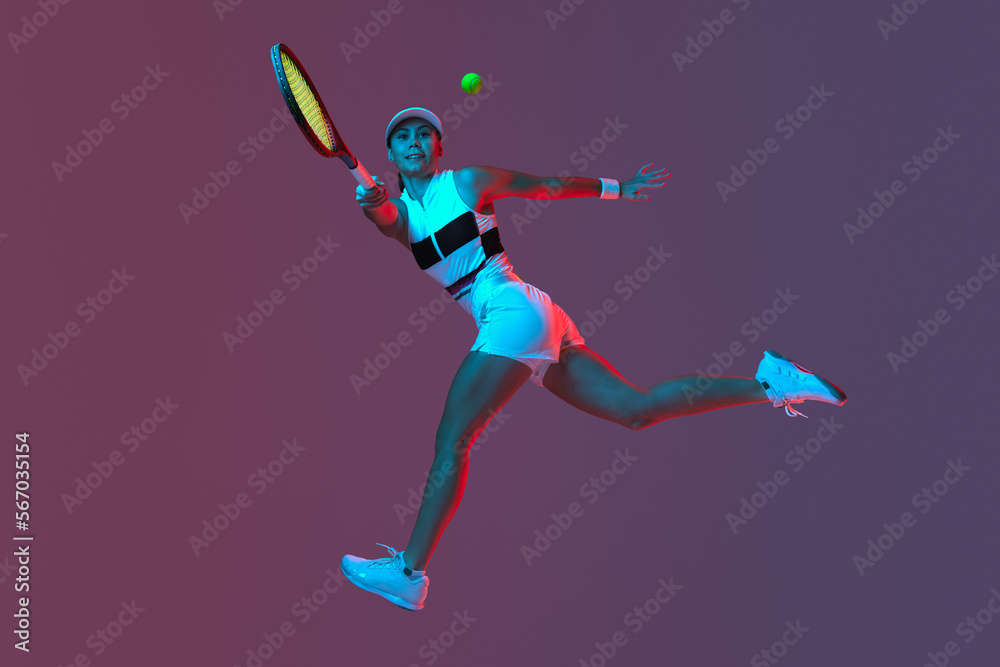 Studio shot of active professional tennis player training with tennis racket over gradient pink-purple background in neon light. Sport, fashion, ad
