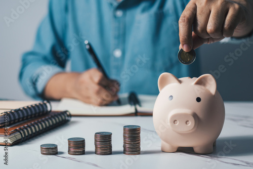 Man putting coins in piggy bank and taking notes in notebook money saving concept business