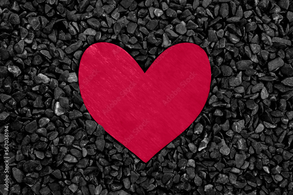 Obraz premium Magenta colored wooden heart on a black stones background