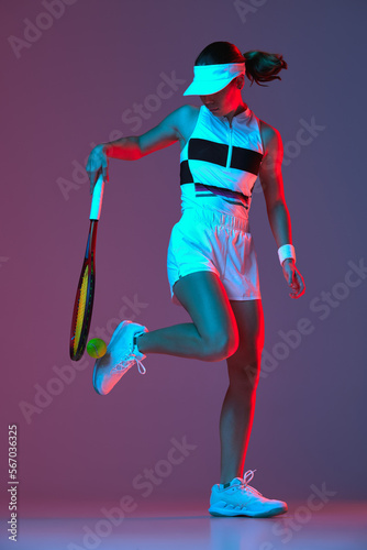 Studio shot of active professional tennis player training with tennis racket over gradient pink-purple background in neon light. Sport, fashion, ad
