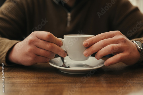 Strong male hands are holding a small white cup with hot beverage in a cafe.