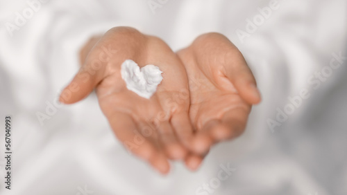 Millennial european woman applying cream on heart shaped on hands, enjoy daily procedures in bedroom