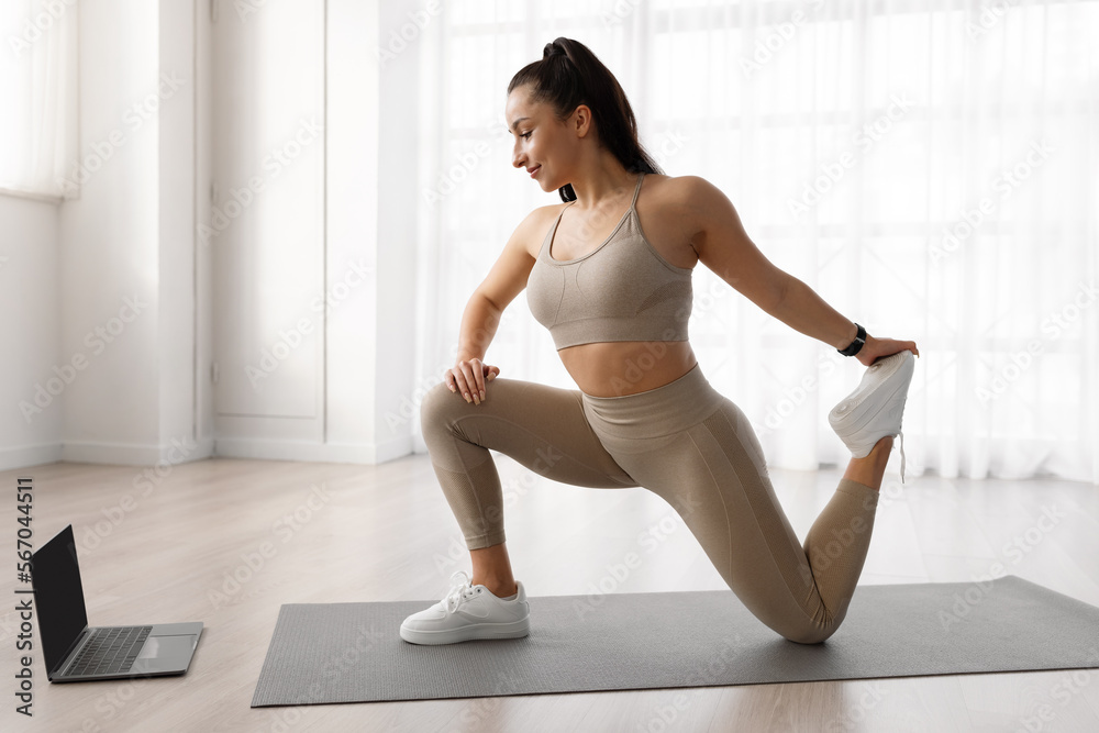 Fototapeta premium Side view of sporty woman training at home, using computer