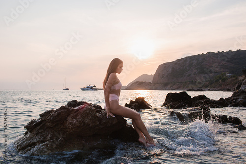 Brown-eyed girl with long hair in a beige bathing suit on the seashore.