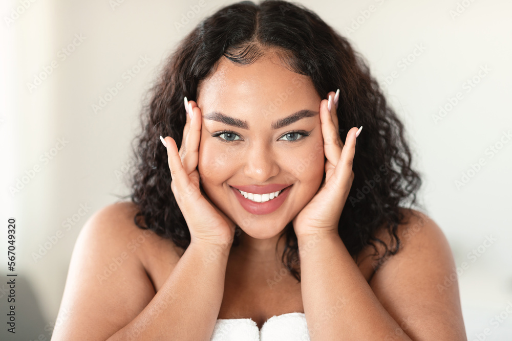 Naklejka premium Facial skincare concept. Happy plus size lady touching face and smiling, enjoying result of new cosmetics
