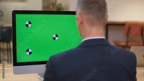 A man in a solid business suit works at a computer. Large monitor with green screen. Shooting an office worker from the back. Official correspondence. A focused leader solves business tasks. Close-up.