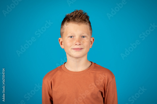 Closeup portrait of smiling preteen boy posing over blue background