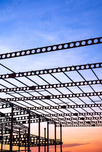 Silhouette of metal castellated beam of factory building structure in construction site against sunset sky background in vertical frame