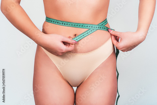 Beautiful slim girl s body with measuring tape around her waist. Photo of woman s body with tanned skin isolated