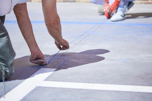 Professional painter at work. Unrecognizable young man uses a rope dipped in blue chalk to mark straight guide lines before apply special acrylic paint for road marking on asphalt.