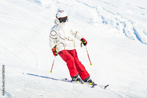 Alpine ski. Skiing woman skier going downhill against snow covered isolated white ski trail slope piste in winter. Good recreational female skier in white ski jacket and red pants