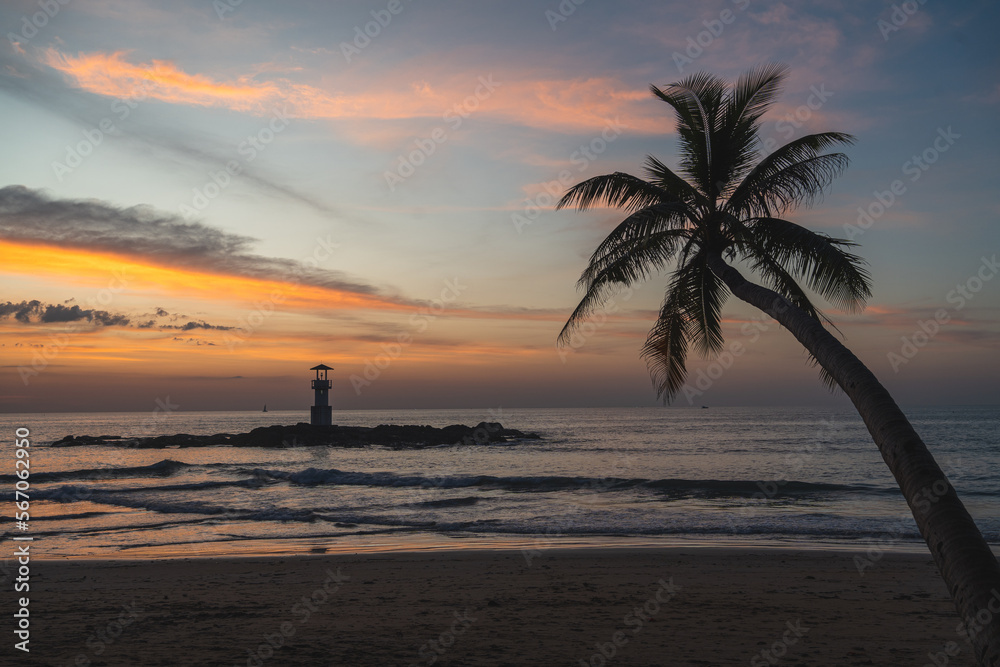 Sunset at Nang Thong Bay in Khao Lak, Thailand. Beautiful colors at the beach with a palm tree in the foreground and a lighthouse at sea.