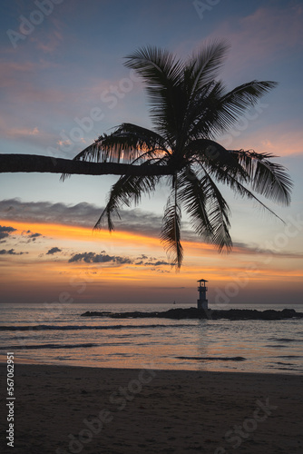 Sunset at Nang Thong Bay in Khao Lak, Thailand. Beautiful colors at the beach with a palm tree in the foreground and a lighthouse at sea.
