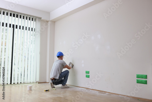 A male builder plasters a white wall in a room photo