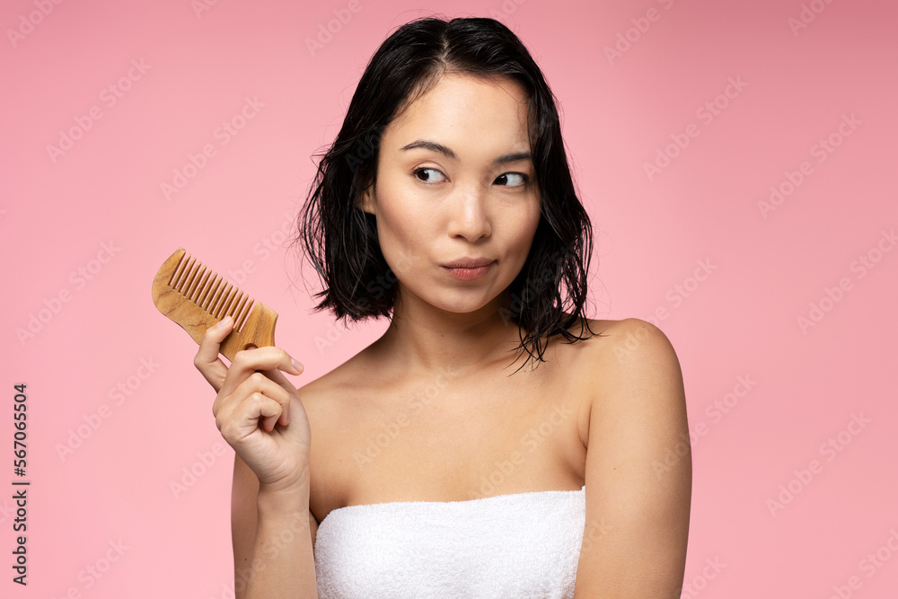 Pensive brunette asian woman with silky chevelure holding wooden hair comb Pensive brunette asian woman with silky chevelure holding wooden hair comb