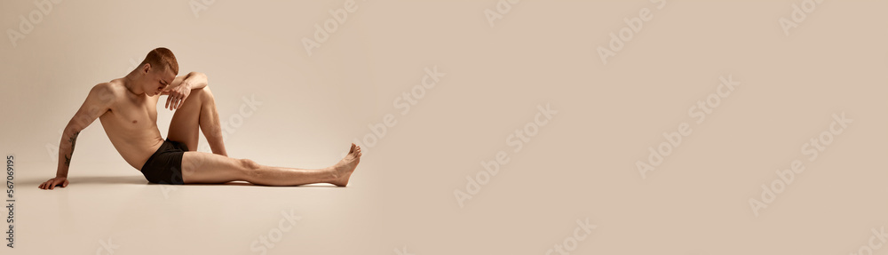 Obraz premium Handsome young man posing in underwear on floor isolated over grey studio background. Muscular, fit male body. Concept of men's health and beauty, body and skin care, fitness. Copy space for ad, text