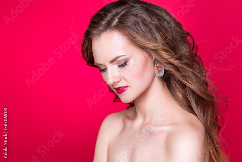 Brunette girl with long wavy hair and beautiful makeup posing in the studio on a red background. The concept of beauty, grace and self-care