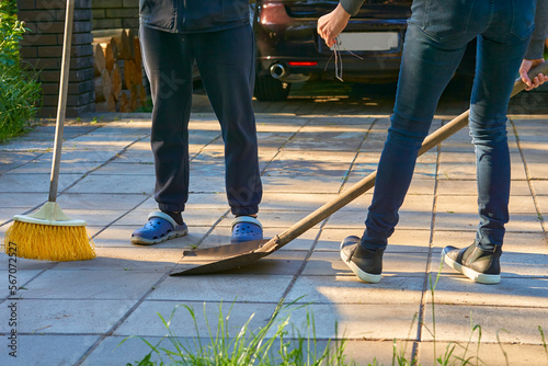 Legs of a man and a woman cleaning the house yard with a shovel and a broom