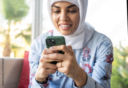 Beautiful Happy Muslim Arabic Woman Using Smartphone Indoors. Concept of social media, online shopping, mobile app