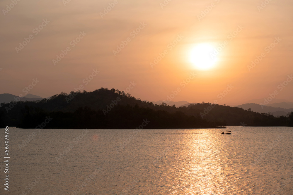 Beautiful sunset behind the mountain silhouette in Kaeng Krachan Reservoir, located in central of Thailand, boat drives in a reservoir far away