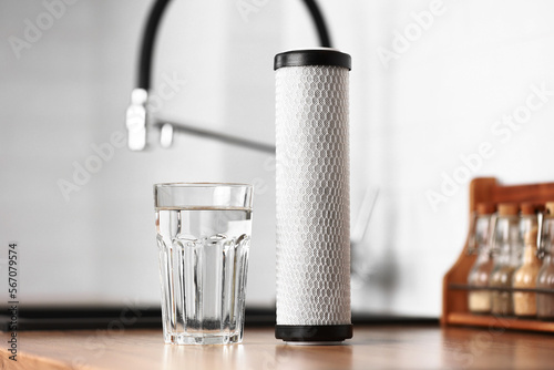 A glass of clean fresh water and carbon filter cartridge on wooden table in a kitchen interior. Installation of reverse osmosis water purification system. Concept Household filtration system.