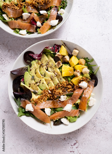 Vertical shoot of healthy salad on a plate with avocado, salmon, lettuce, cheese and mango on a stone tabvle
